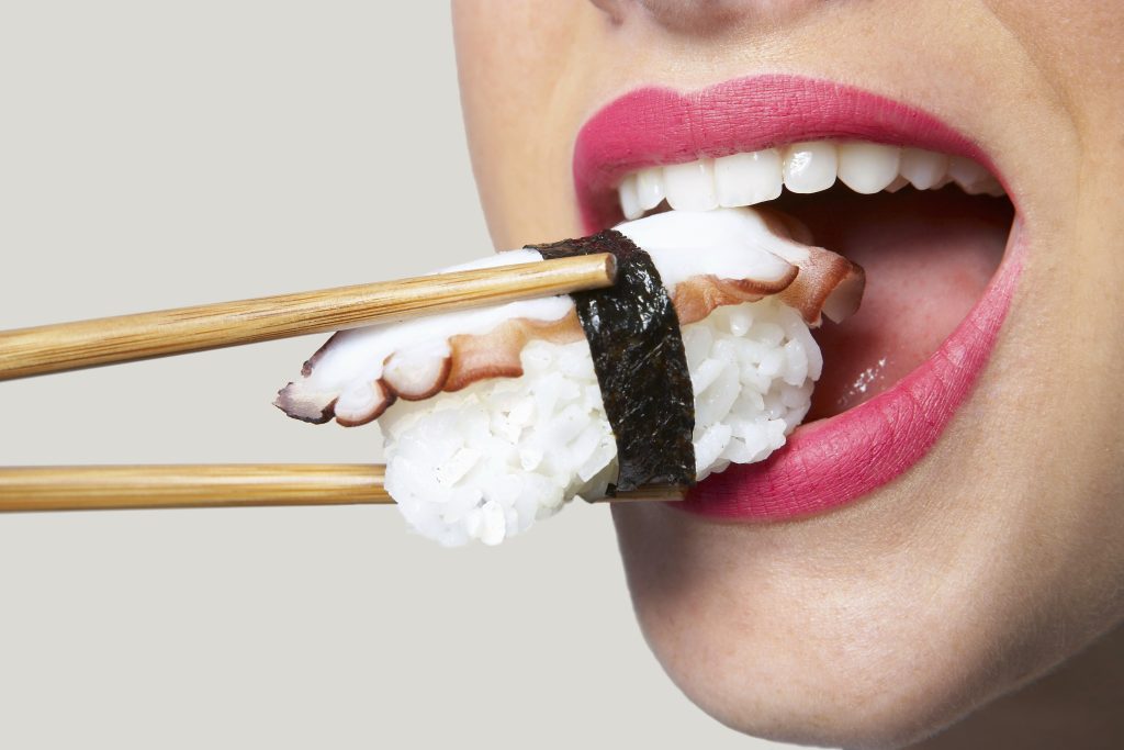 Kobieta, która wkłada do ust sushi.