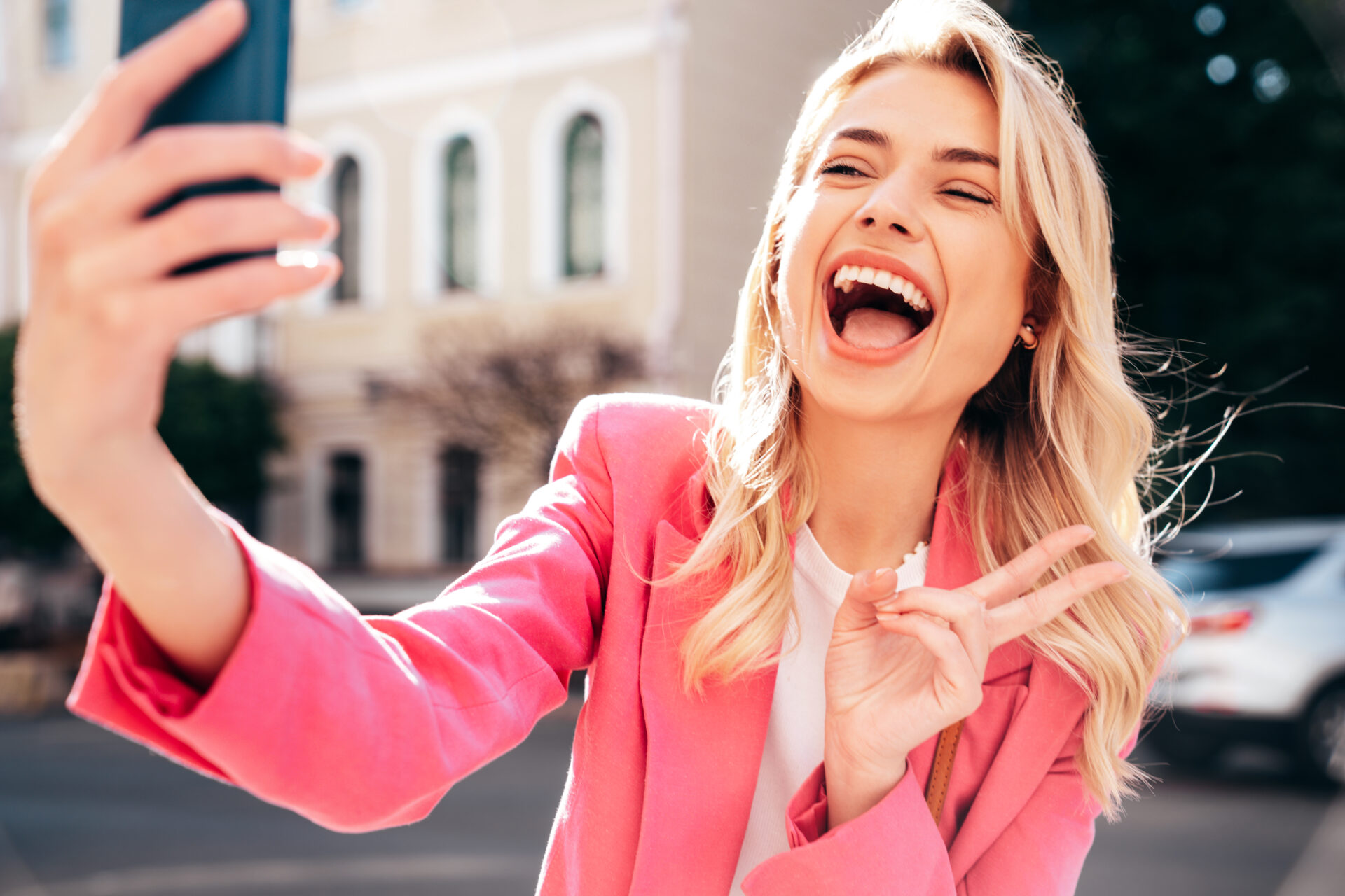 Uśmiechnięta młoda kobieta robiąca selfie telefonem na tle miejskiej ulicy.