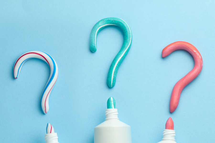 Trzy tubki z wyciśniętą pastą do zębów w różnych kolorach, która układa się w znaki zapytania